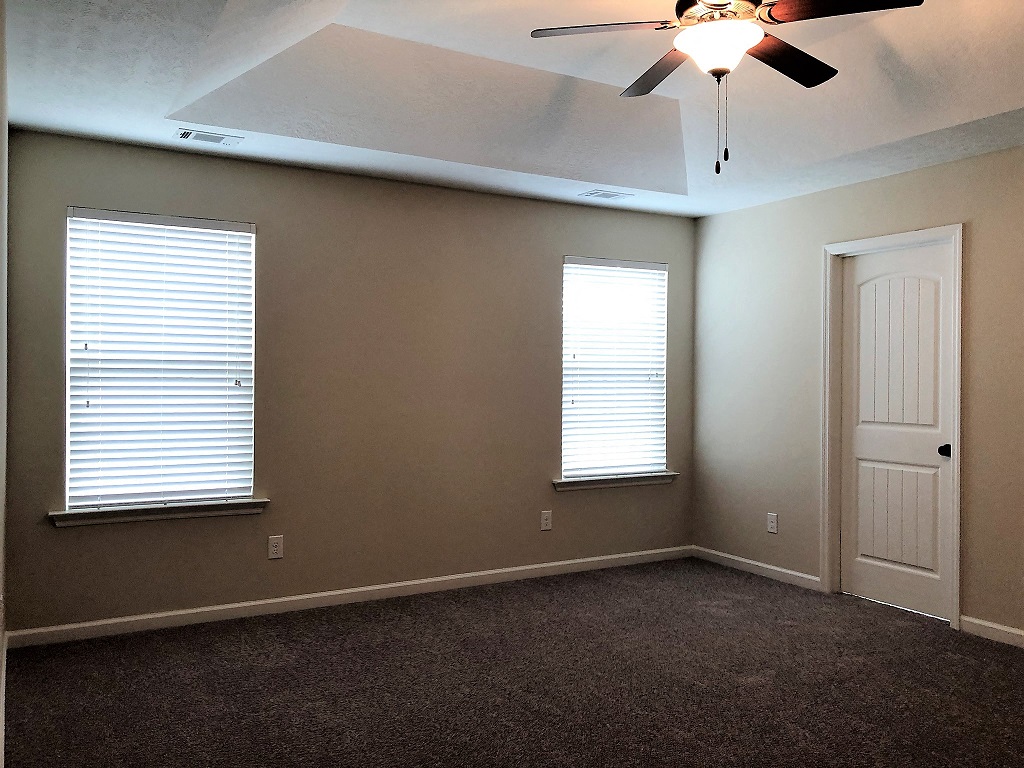 A room with a ceiling fan and two windows.